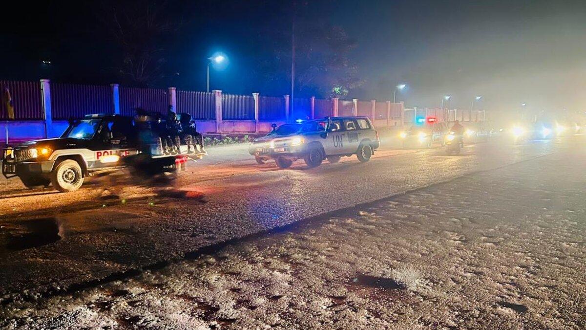 Des véhicules de l'ONU et de la police circulent sur une route de nuit.