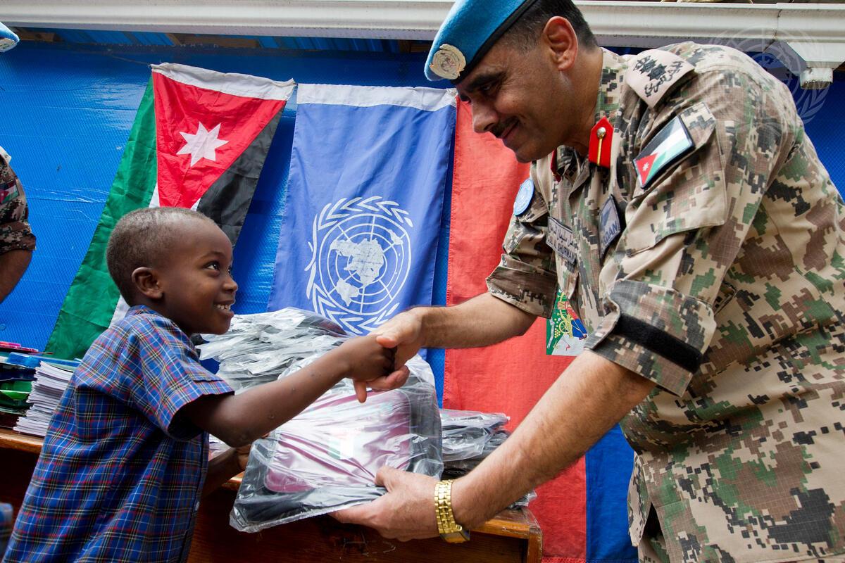 A Jordanian peacekeeper shakes hands with a young Haitian boy.